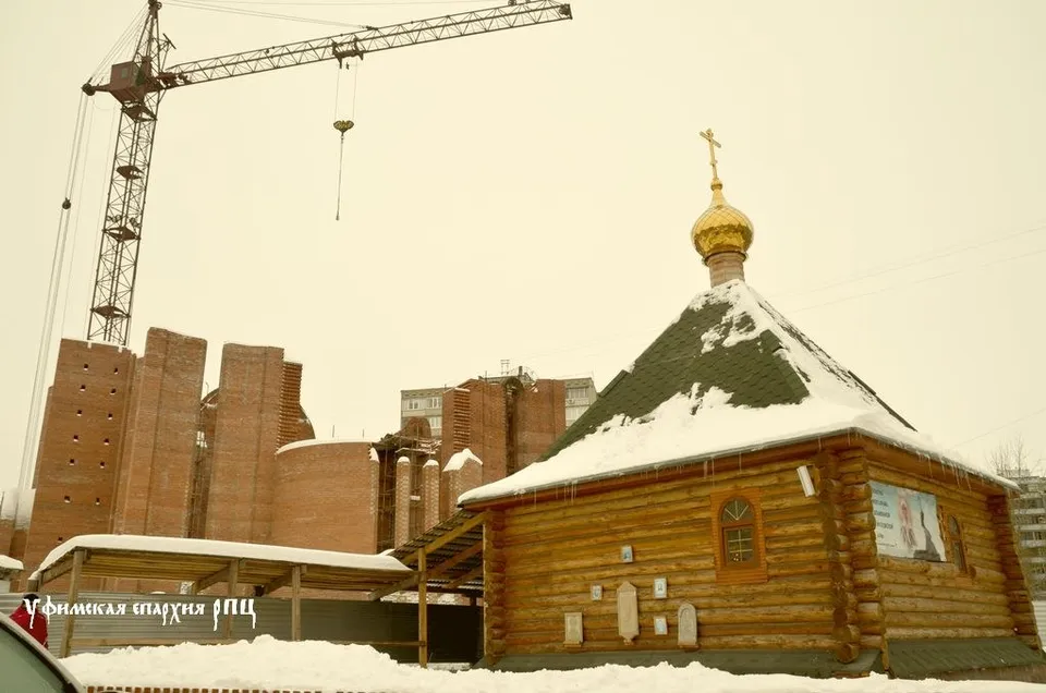 Строящееся здание храма с деревянной обшивкой стен, одной золотой главой с крестом и строительным краном на площадке