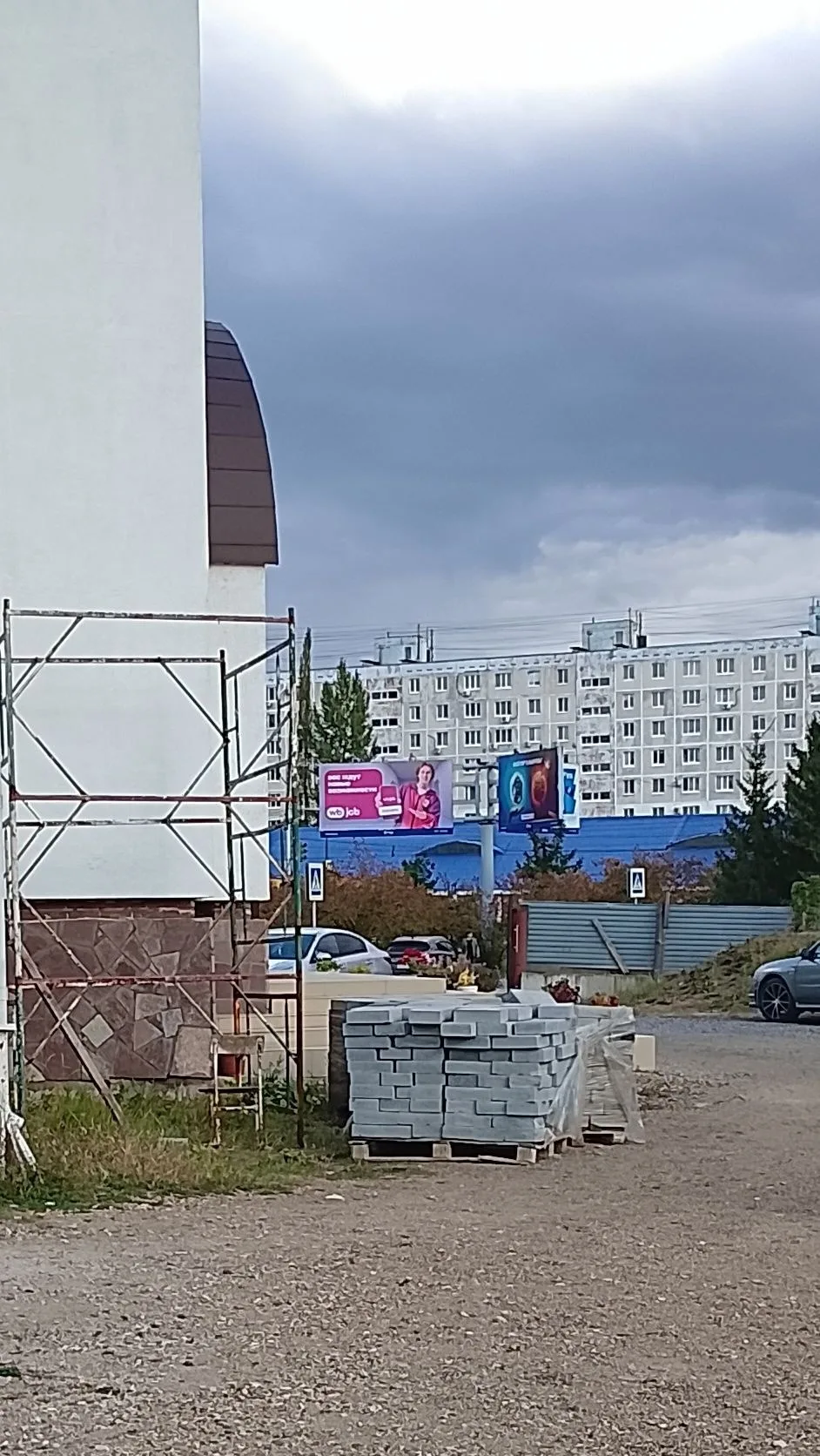 Угол белого храма с декоративной каменной облицовкой цоколя, вдали — жилые высотки и рекламные щиты