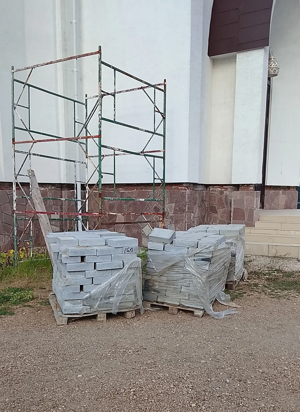 Старые строительные леса и упакованная в плёнку тротуарная плитка у белой стены храма